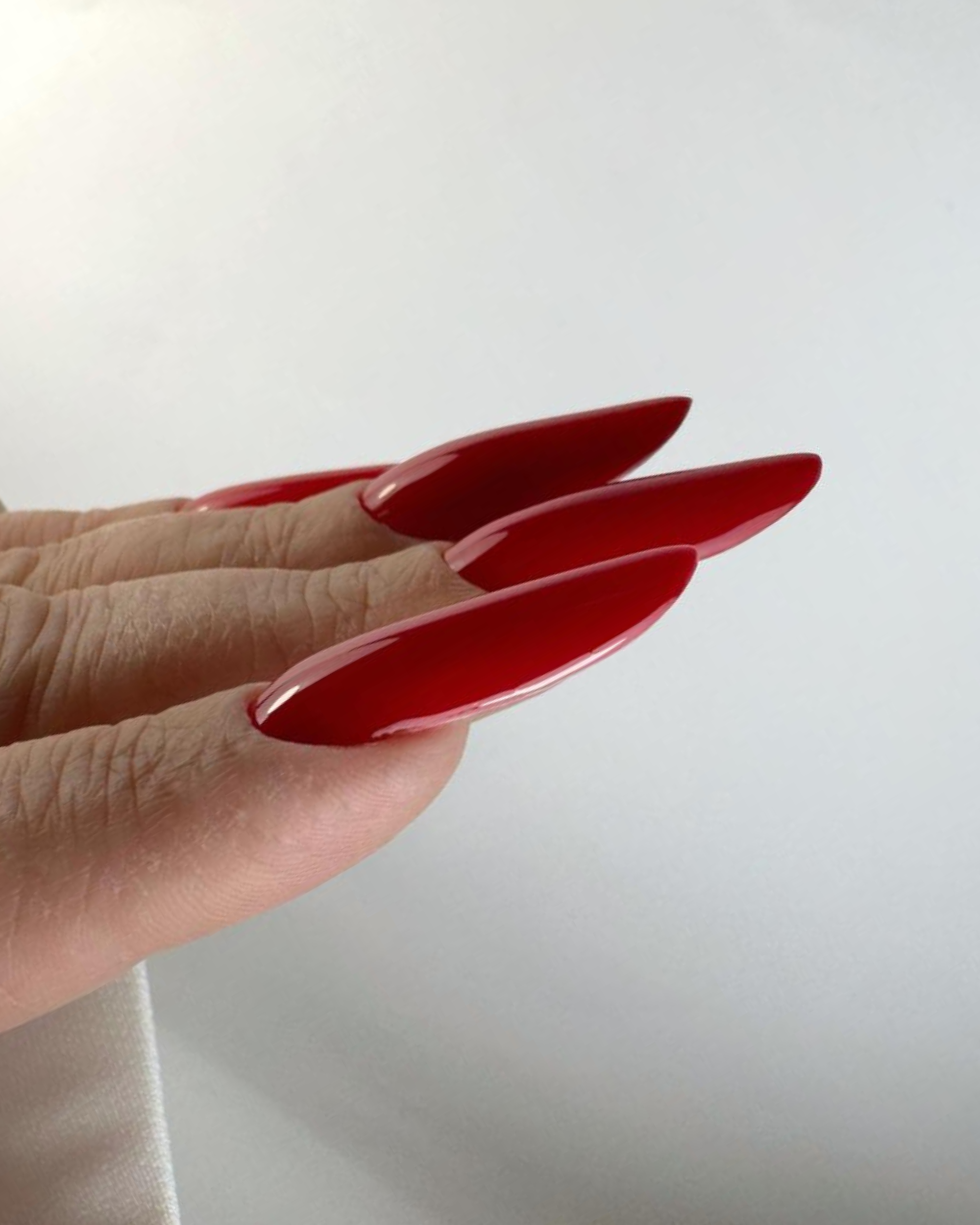 side view of red almond gel nails showing correct apex and structure – Twinz Nails training technique